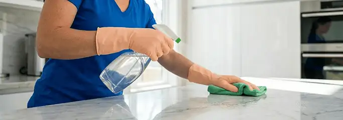 Maid service worker spraying and wiping a kitchen countertop with a microfiber cloth for sanitizing, Boston, MA.